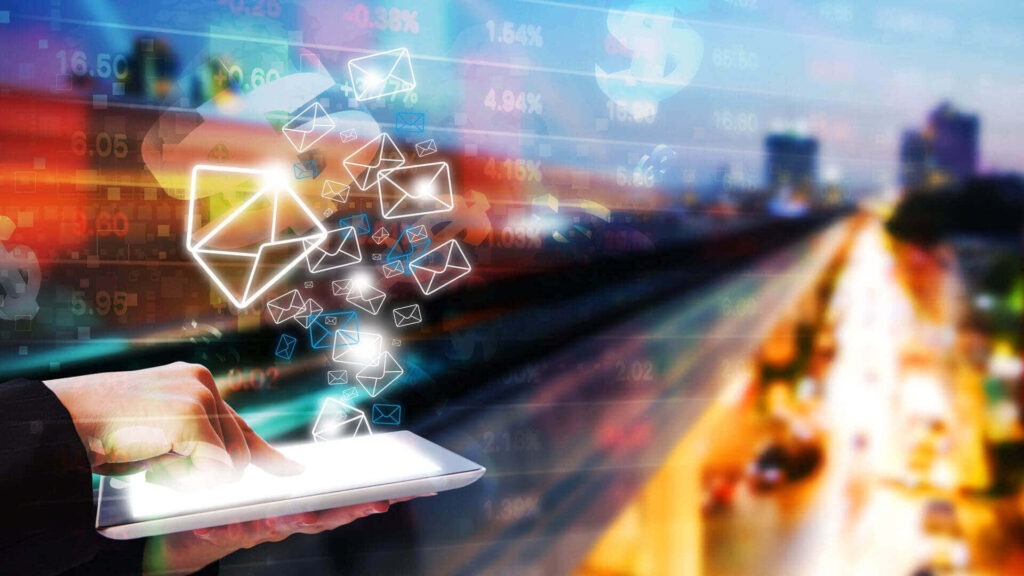 Person using tablet emitting glowing email icons over vibrant blurred cityscape digital communication background Wallpaper