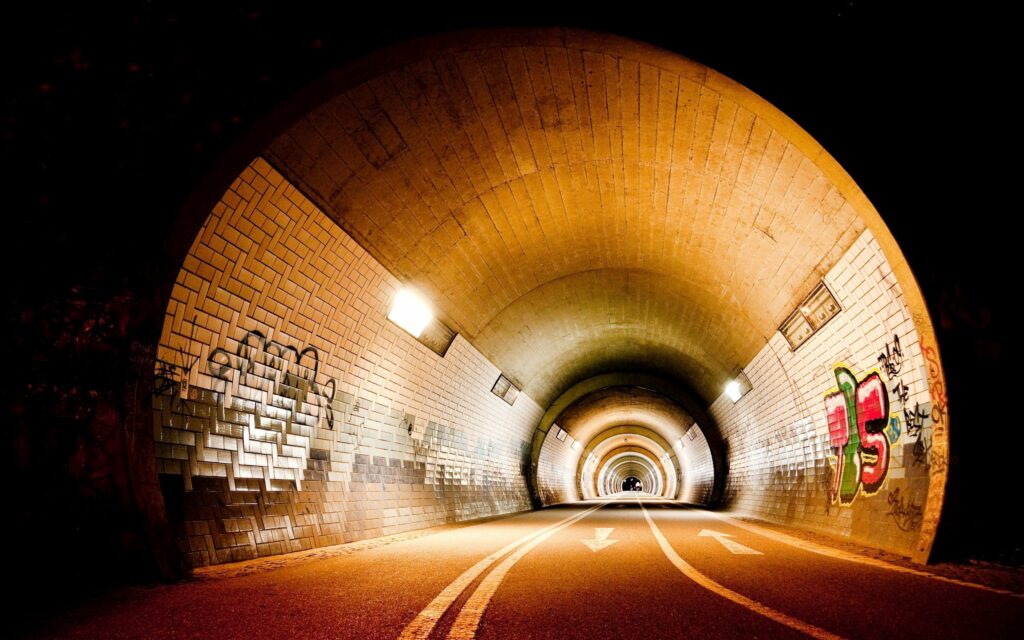 Dimly Lit Tunnel Wallpaper: Graffiti Walls & Warm Light Ambiance