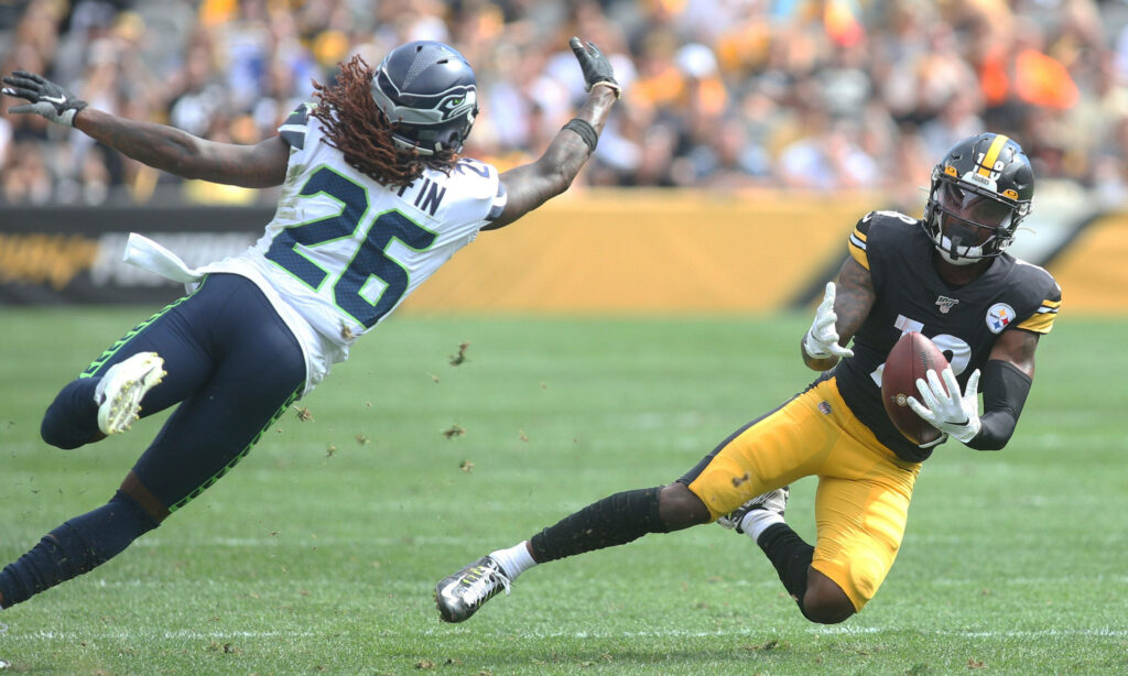 Diontae Johnson catching football in Steelers uniform chased by Seahawks defender stadium background Wallpaper