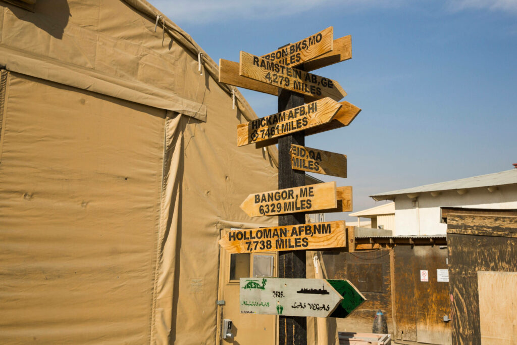 Directional arrow signs at Bagram Airbase Afghanistan with military tents under clear sky wallpaper