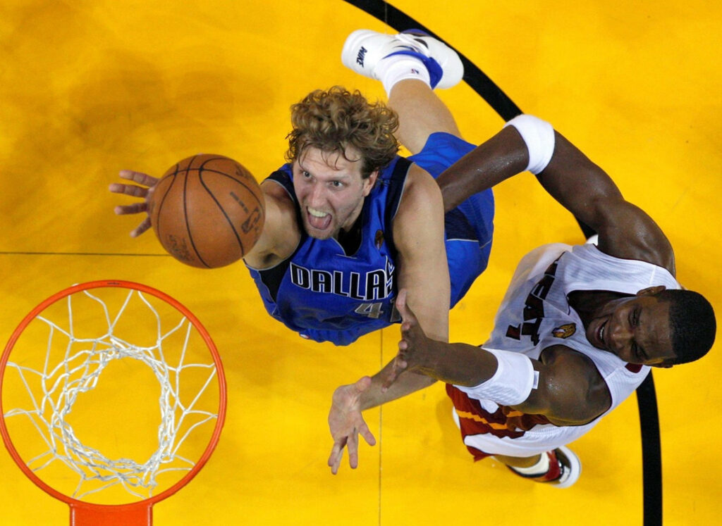 Dirk Nowitzki in Dallas Mavericks jersey jumps for rebound vs Miami Heat on vibrant court overhead Wallpaper