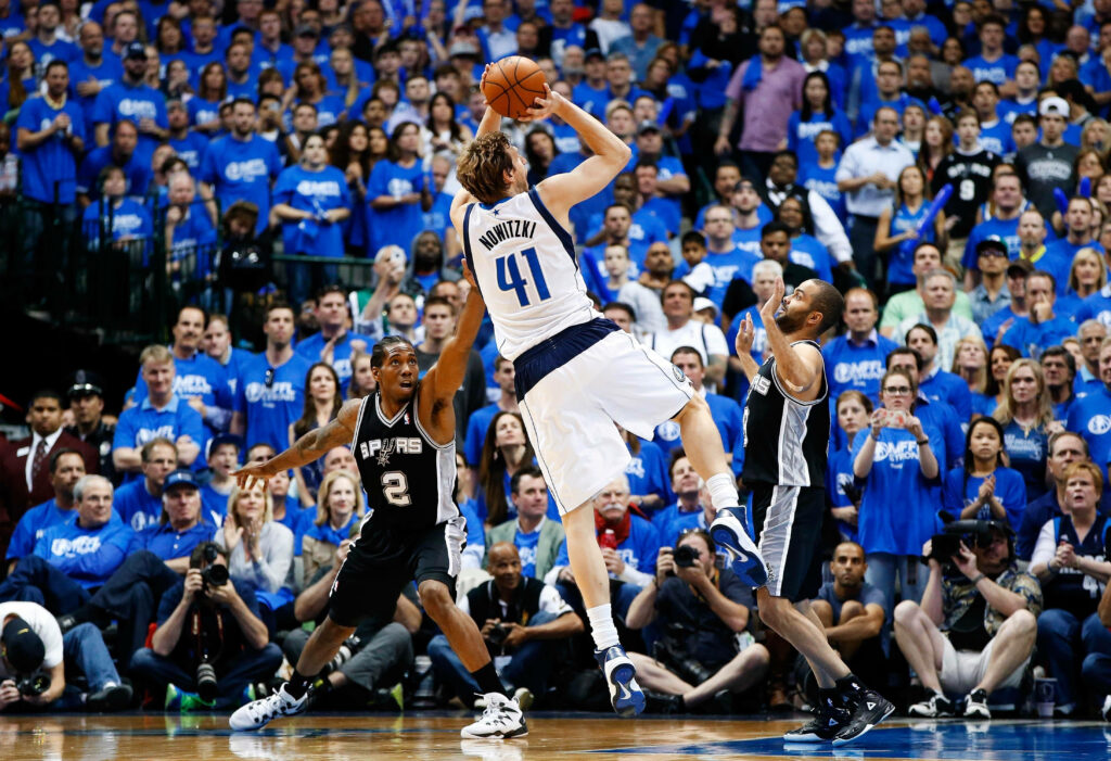 Dirk Nowitzki fadeaway jump shot against Spurs defenders in vibrant packed arena wallpaper background
