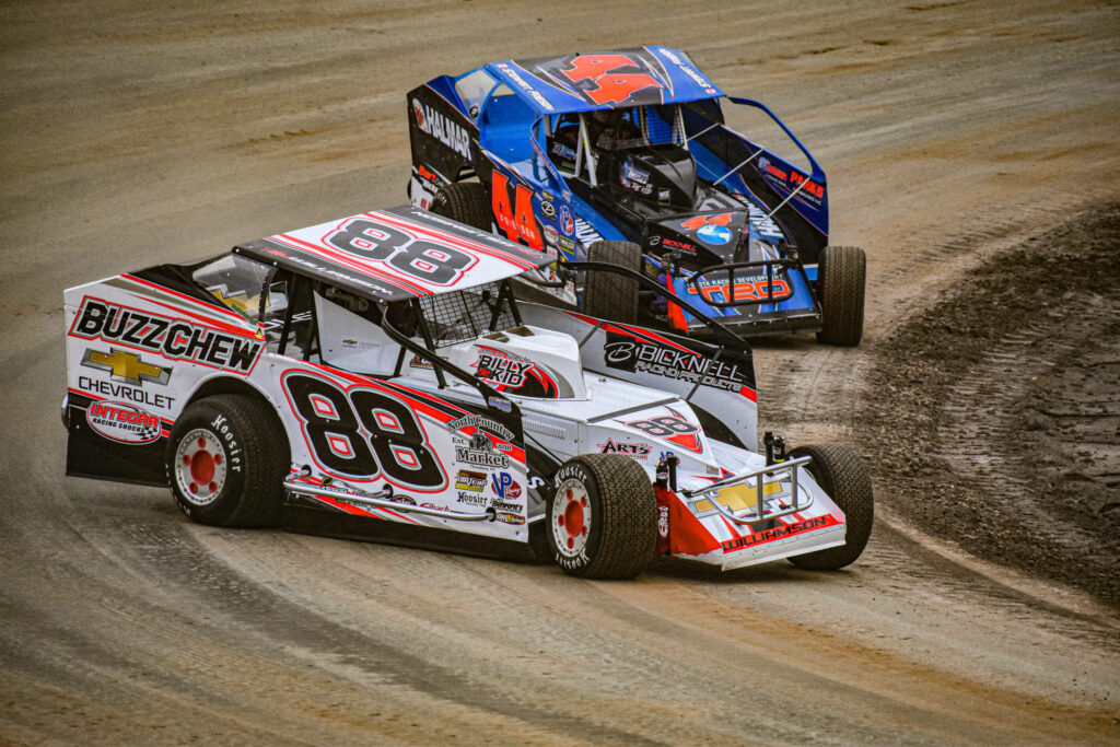 Two modified dirt race cars 88 white red and 44 blue speeding on dusty track wallpaper background