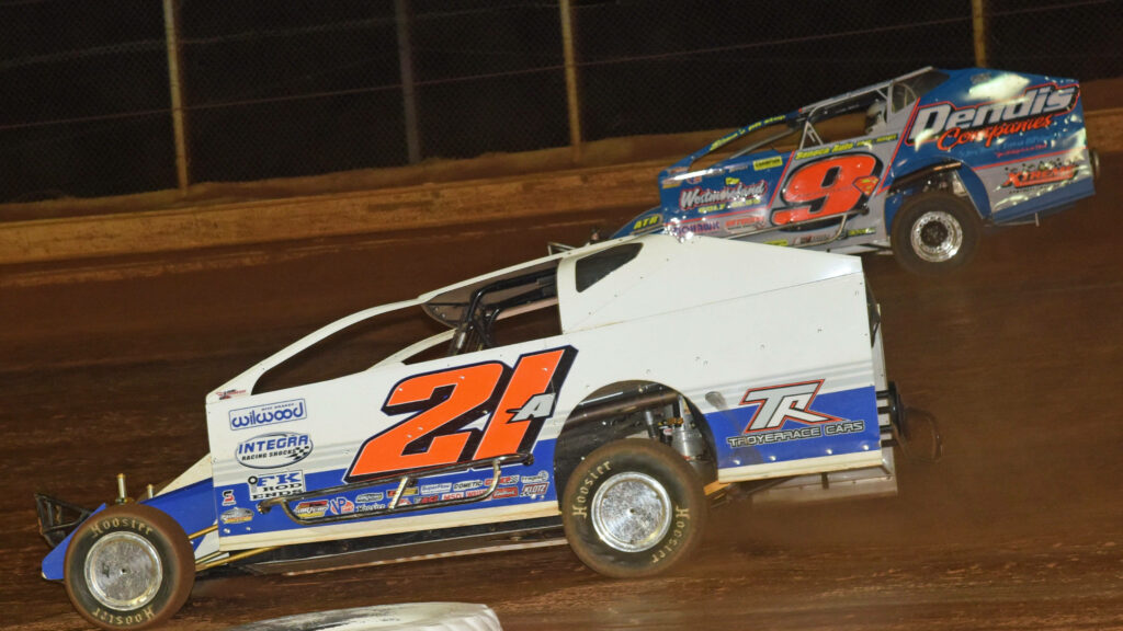 Two dirt track race cars speeding on oval track kicking up dust with vibrant decals wallpaper