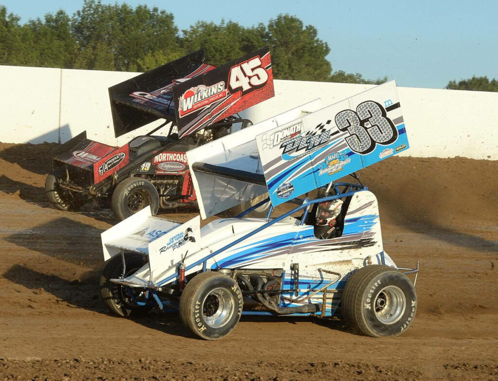 Two sprint cars racing on dirt track dust flying blue white car 33 leads red black car 45 Wallpaper