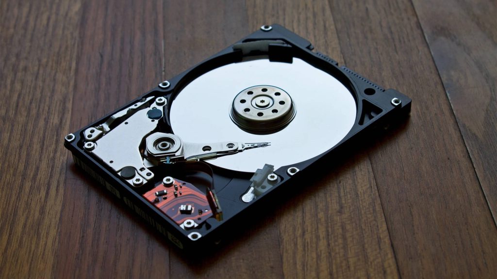 High-angle view of a disassembled internal hard disk drive on rustic wood surface detailed platter Wallpaper