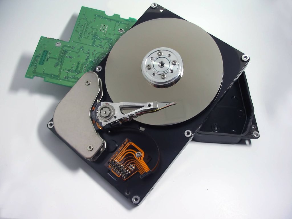 Top view of disassembled hard disk drive showing metallic platter actuator arm and green PCB board Wallpaper