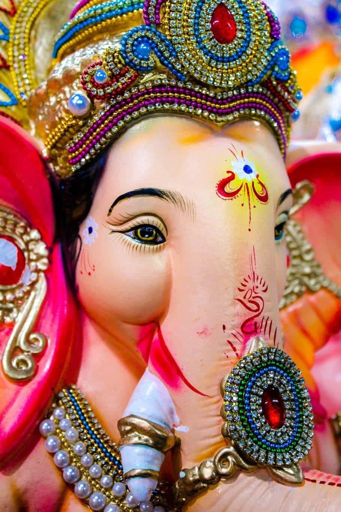 Close-up of vibrant Lord Ganesha idol with ornate gem crown and intricate golden jewelry wallpaper
