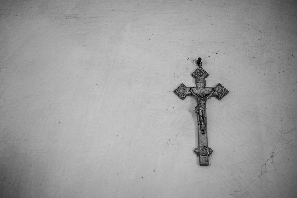 Sacred Savior: A Silver Cross Bearing the Crucifixion of Jesus Finds Solitude Against a Dusty Gray Wall Wallpaper