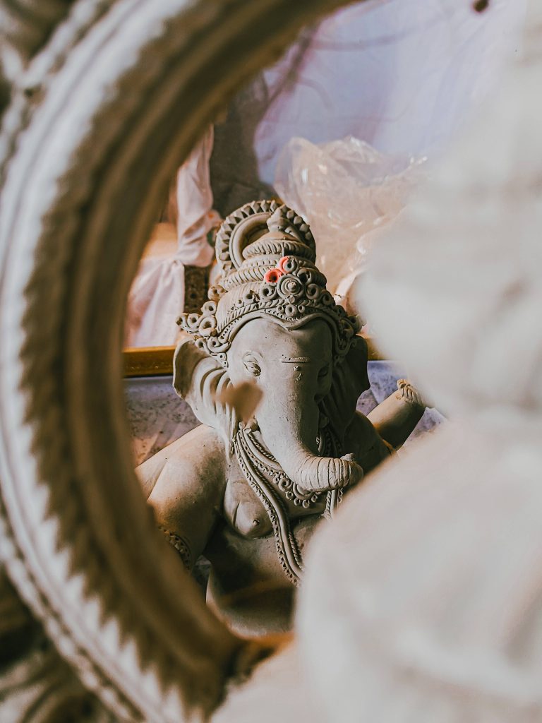 Unpainted clay Ganesh idol viewed through circular frame soft light earthy devotional wallpaper