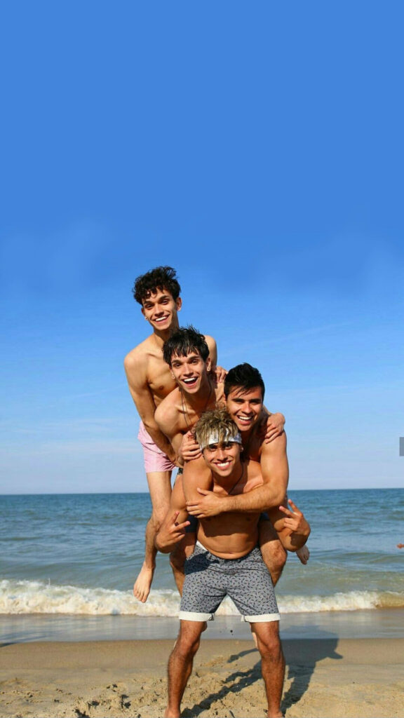 Dobre Brothers stacked playfully on beach with blue sky ocean waves sunny youthful vibrant energy wallpaper