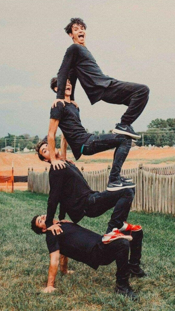 Dobre Brothers human pyramid on grass field in black outfits showing teamwork and acrobatics Wallpaper