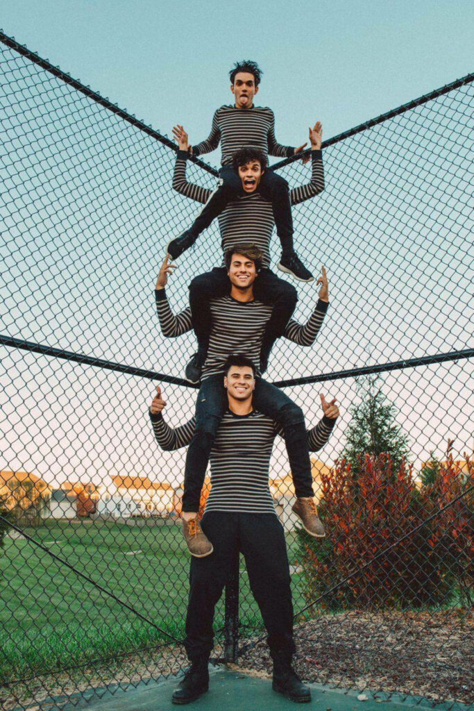 Dobre Brothers stacked playfully outdoors in matching striped shirts with greenery background Wallpaper