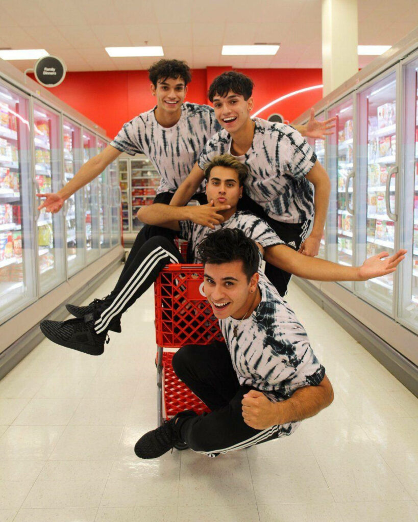 Dobre Brothers in matching tie-dye shirts posing joyfully in bright modern grocery store aisle Wallpaper