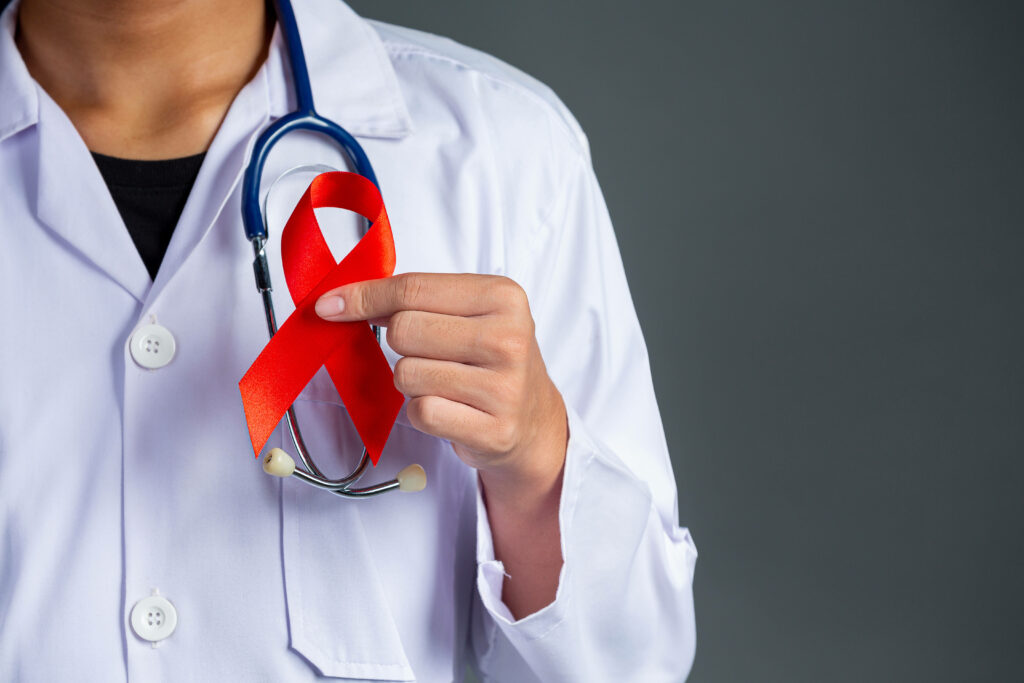 Doctor in white coat holding red health awareness ribbon with stethoscope on gray background Wallpaper
