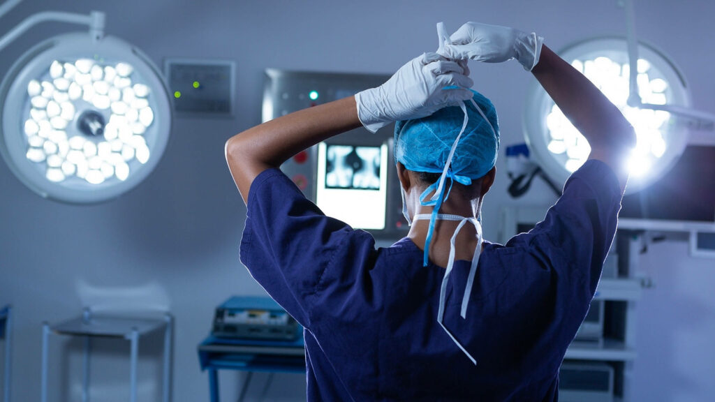 Doctor in modern operating room tying face mask with gloves high tech sterile medical setting Wallpaper