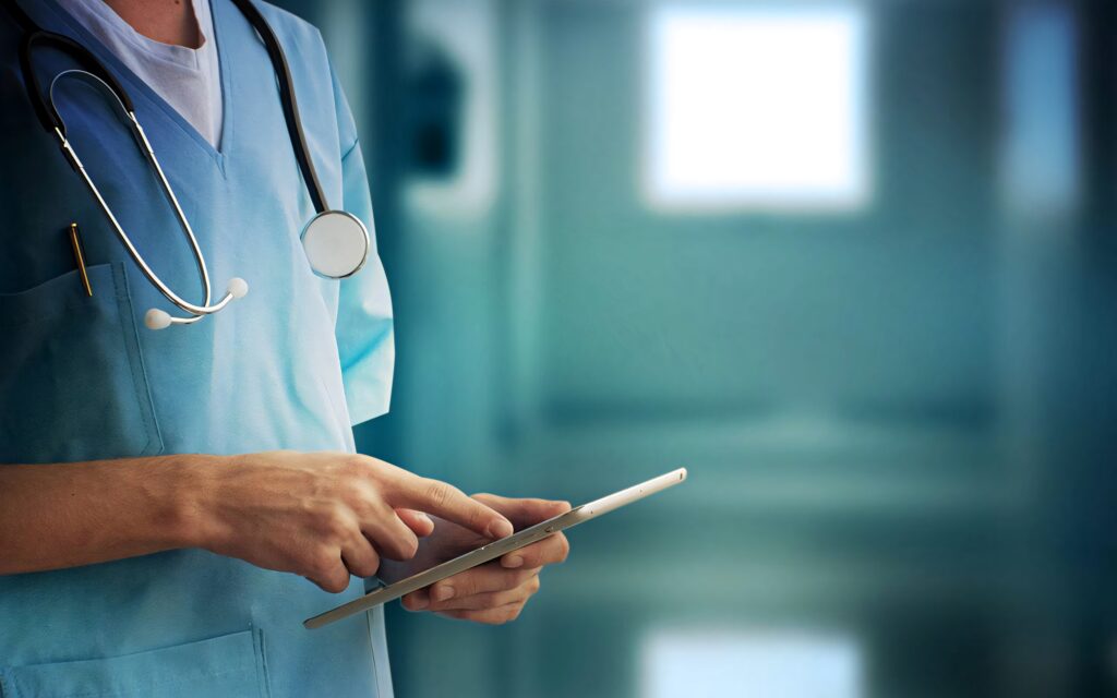 Doctor in blue scrubs with stethoscope using tablet in modern hospital corridor with blue tones Wallpaper