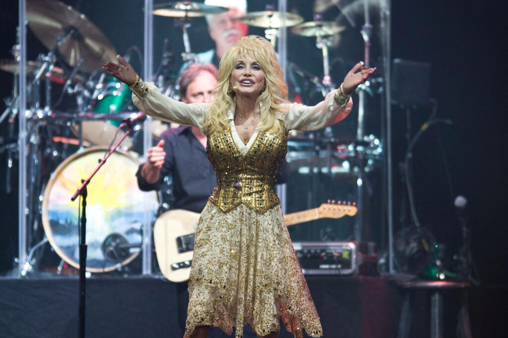 Dolly Parton performing live in sparkling gold vest and patterned dress on vibrant concert stage Wallpaper