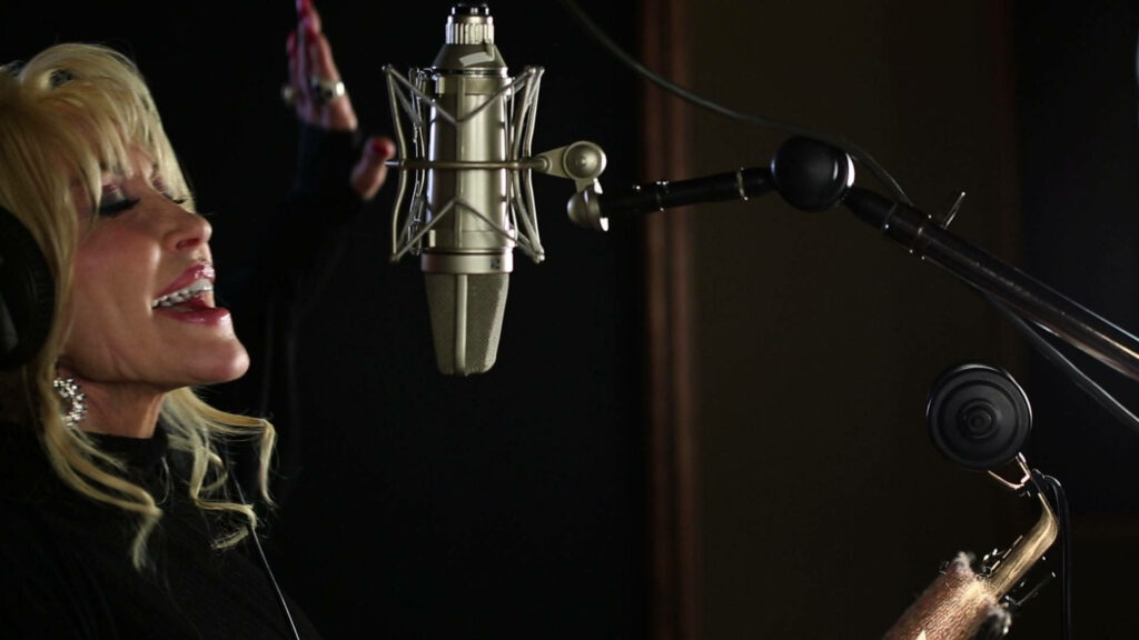 Dolly Parton singing passionately in warm lit professional music studio with condenser microphone Wallpaper