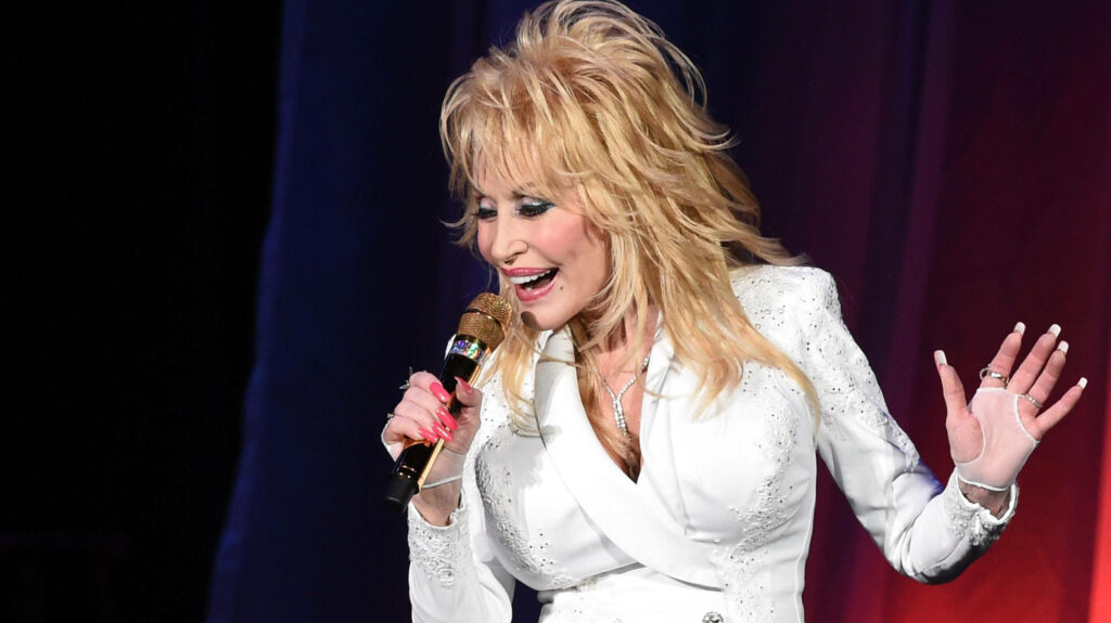 Dolly Parton singing passionately onstage in white sparkling outfit colorful country music wallpaper