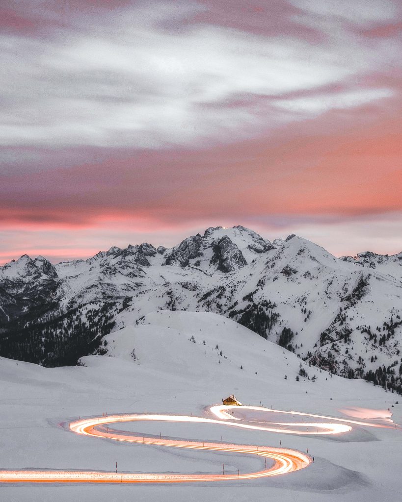 Dolomites winter twilight with glowing vehicle light trails and snowy mountains cozy refuge Wallpaper