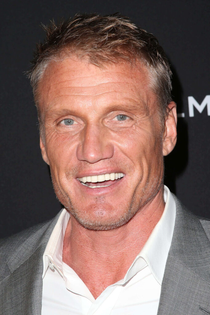 Dolph Lundgren close-up portrait with confident smile rugged features sharp suit dark background Wallpaper