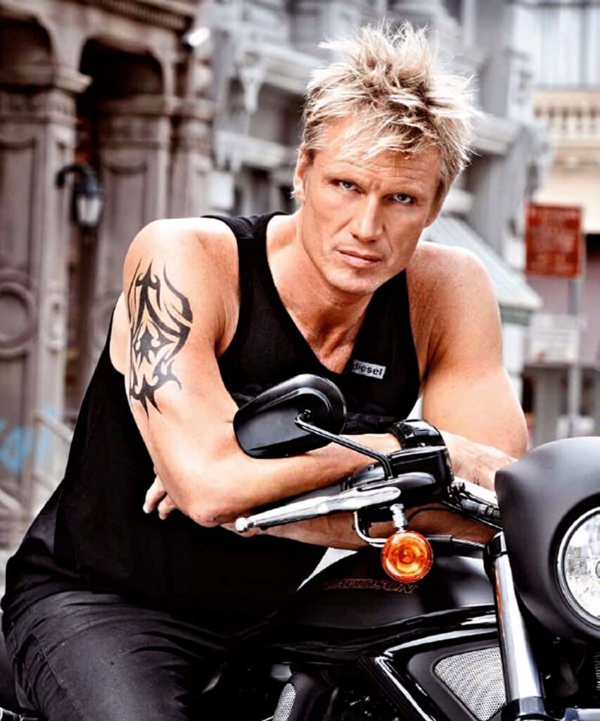 Dolph Lundgren on motorcycle with tattoo sleeveless black shirt urban city backdrop wallpaper