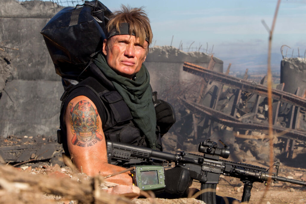 Dolph Lundgren in tactical gear in gritty action scene with battlefield debris and dramatic lighting Wallpaper