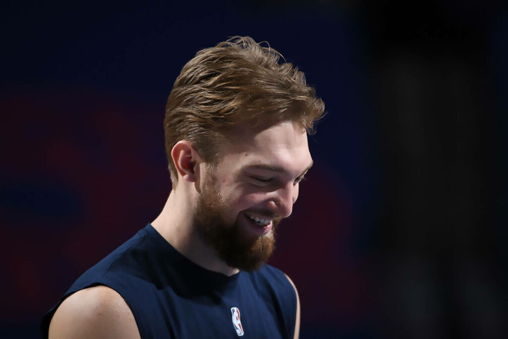 Domantas Sabonis smiling warmly in natural light with dark blue wallpaper background basketball star