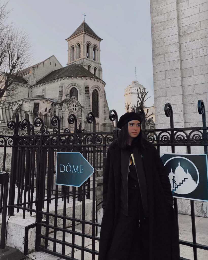 Domelipa in black winter outfit and beret by historic stone architecture and iron railings Wallpaper