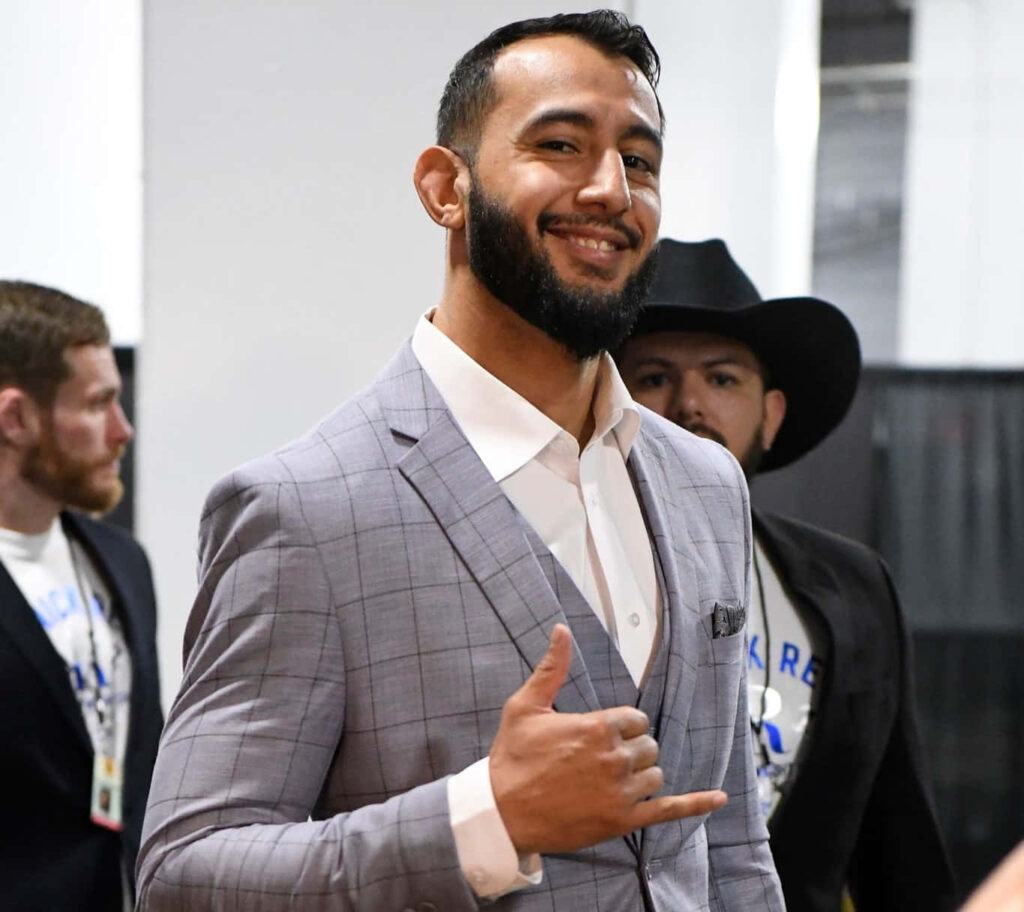 Dominick Reyes confident smile thumbs up light gray plaid suit professional indoor background Wallpaper