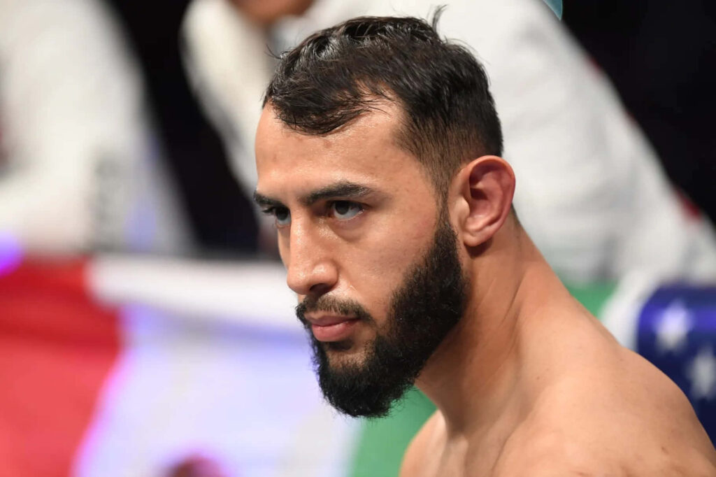 Close-up of MMA fighter Dominick Reyes focused during fight with blurred crowd and flags background Wallpaper