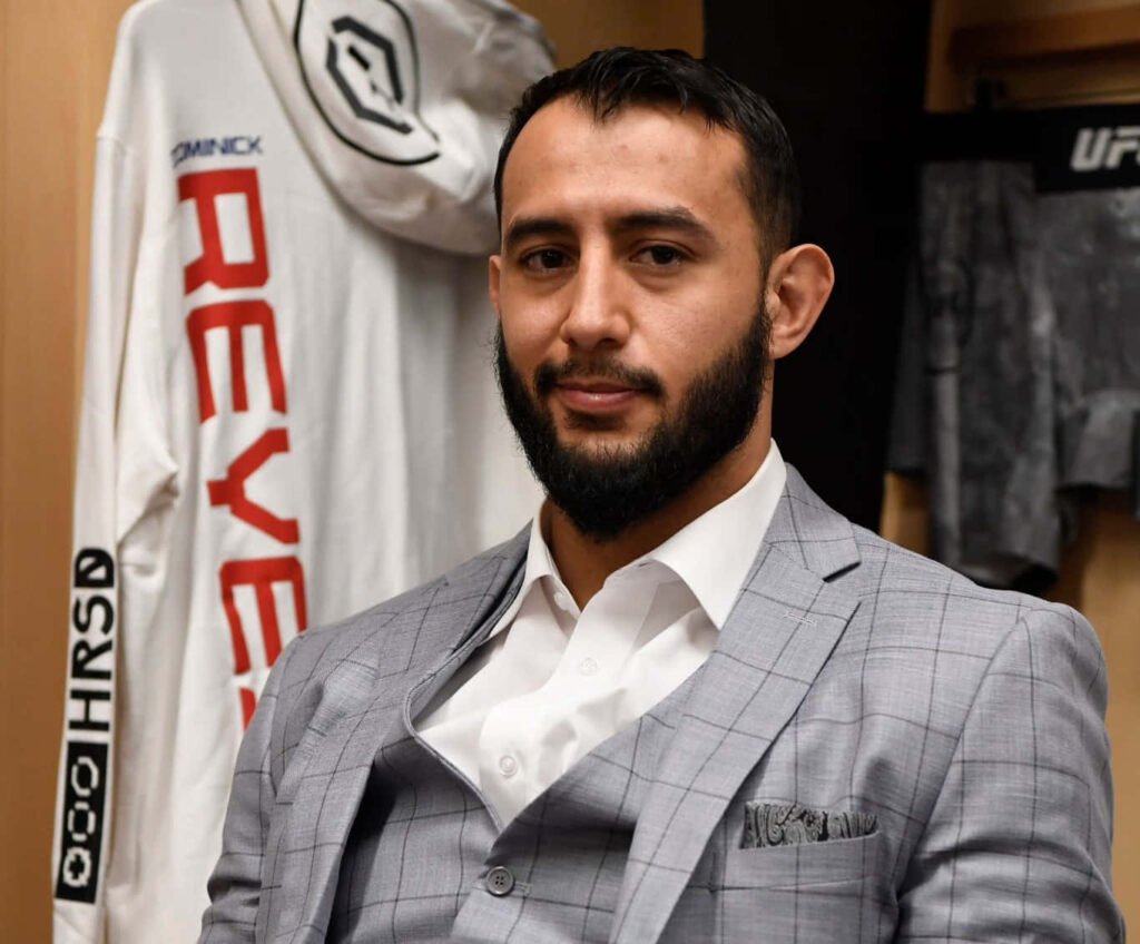 Dominick Reyes in light gray checkered suit with UFC gear background showcasing MMA fighter style Wallpaper