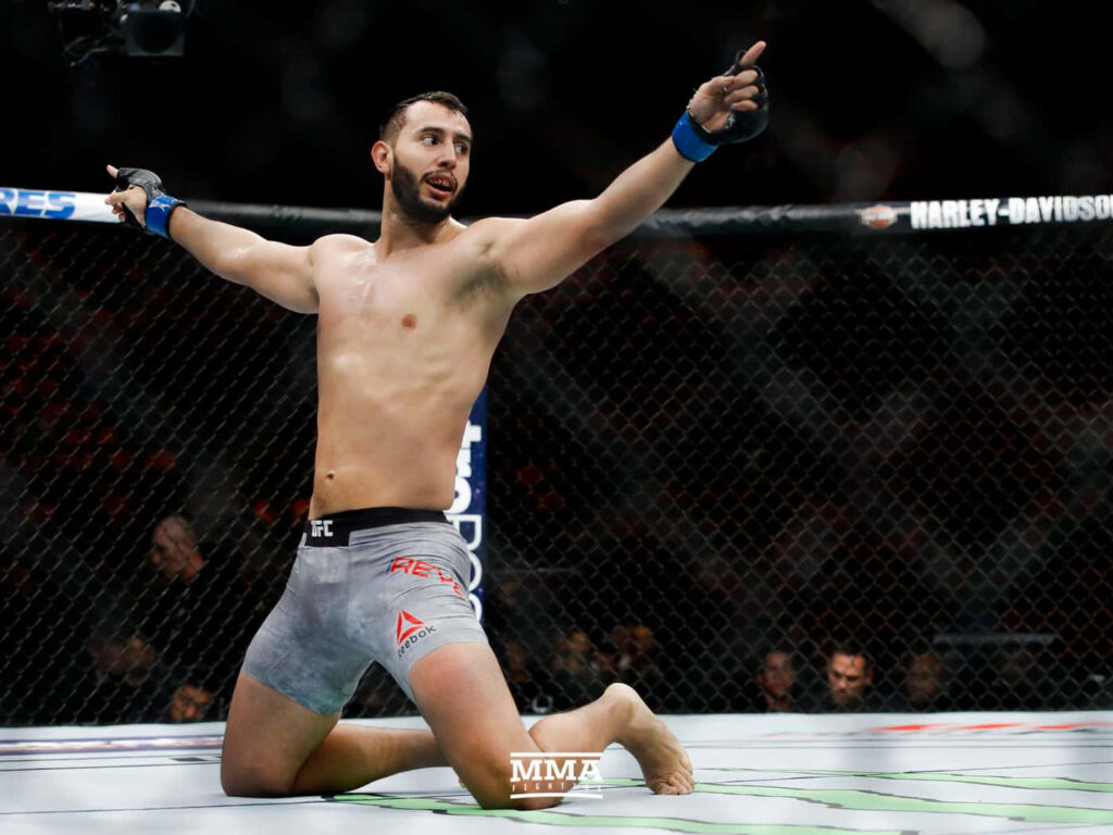 Dominick Reyes UFC victory pose on one knee arms raised in octagon with cage and crowd background Wallpaper