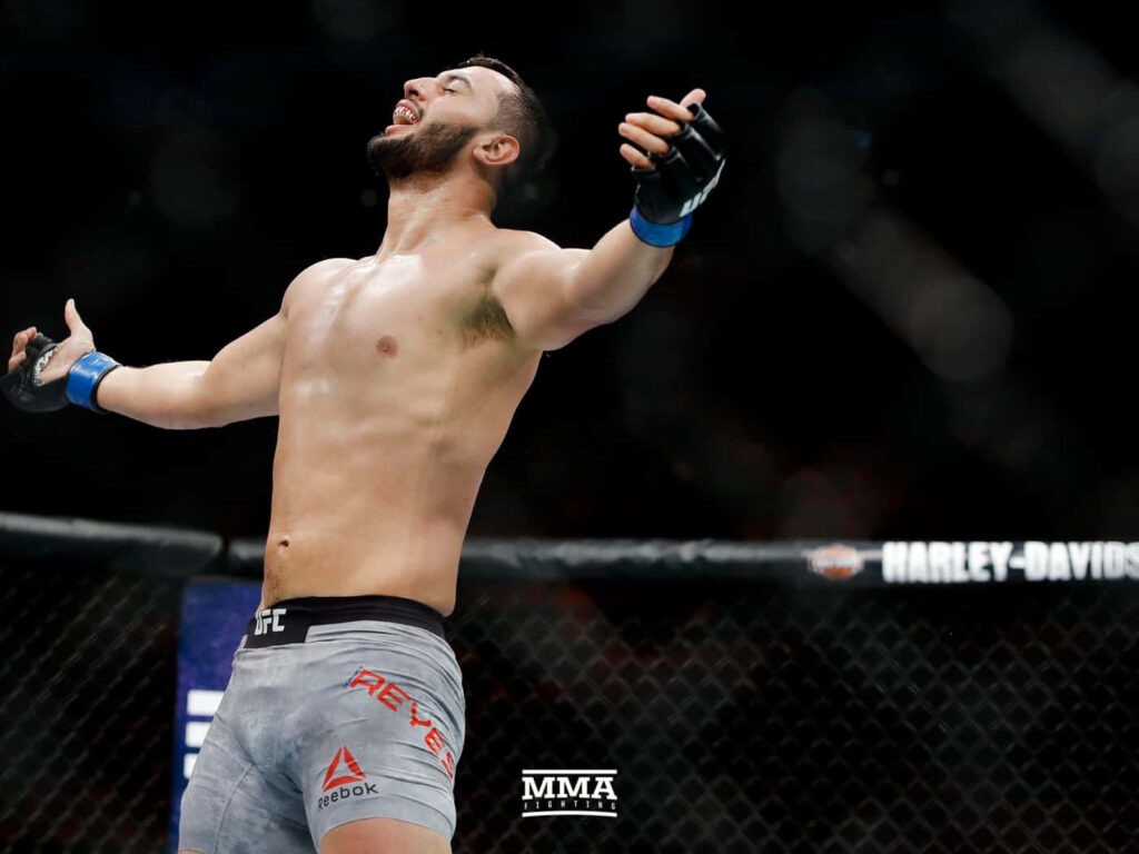 Dominick Reyes victorious in MMA octagon raising arms triumphant showcasing athletic strength Wallpaper