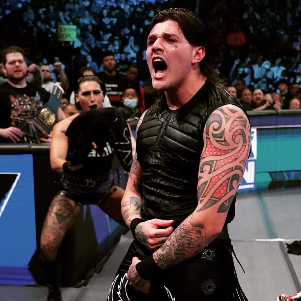 Dominik Mysterio shouting in wrestling ring wearing black gear with tattoo sleeve and crowd background Wallpaper