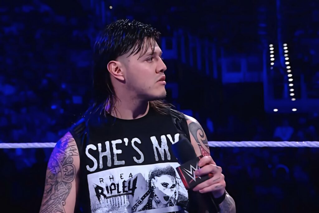 Dominik Mysterio in WWE ring wearing She's My Rhea Ripley shirt under vibrant blue arena lights Wallpaper