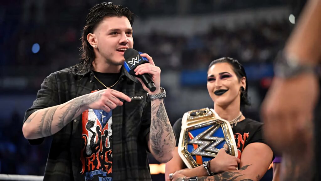 Dominik Mysterio speaking passionately with Rhea Ripley holding WWE championship belt at event Wallpaper
