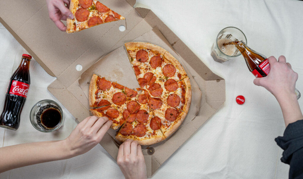 Top view of Domino's pepperoni pizza with hands grabbing slices and glasses of Coca Cola Wallpaper