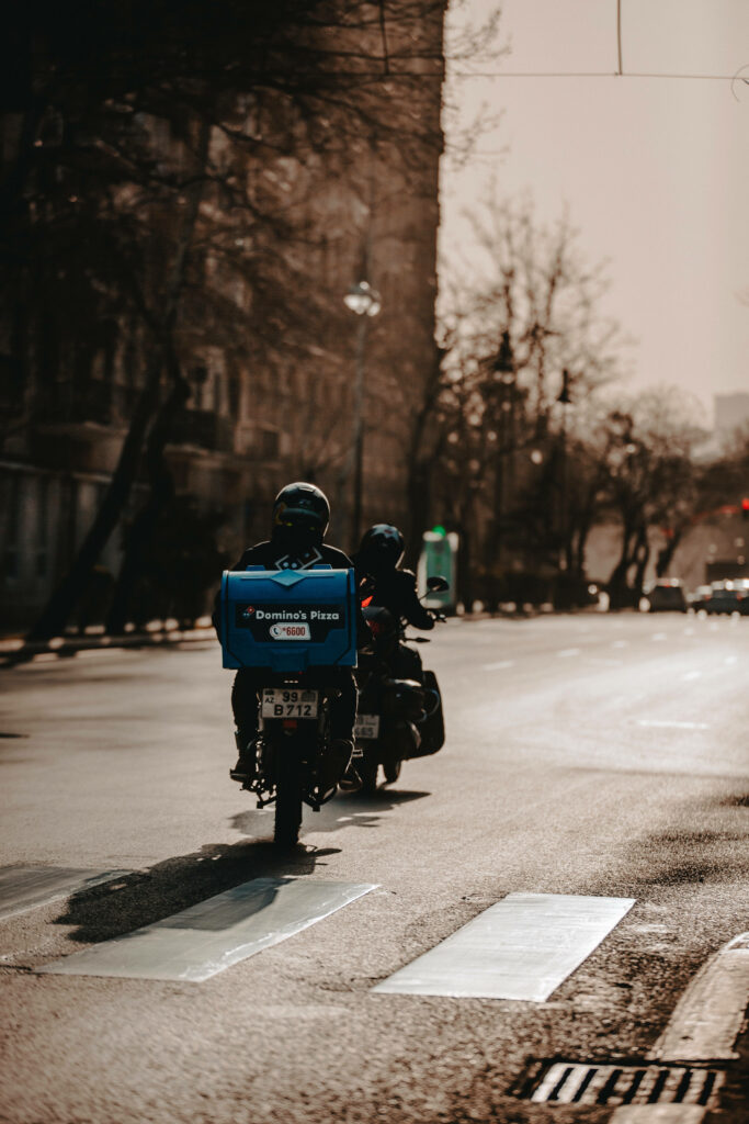 Dominos Pizza delivery rider on motorbike at sunset urban street with blue pizza box shadows Wallpaper
