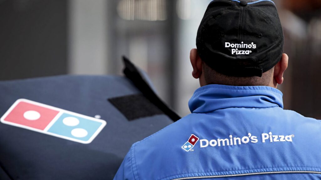 Dominos Pizza delivery staff in blue uniform handling pizza bag urban setting wallpaper