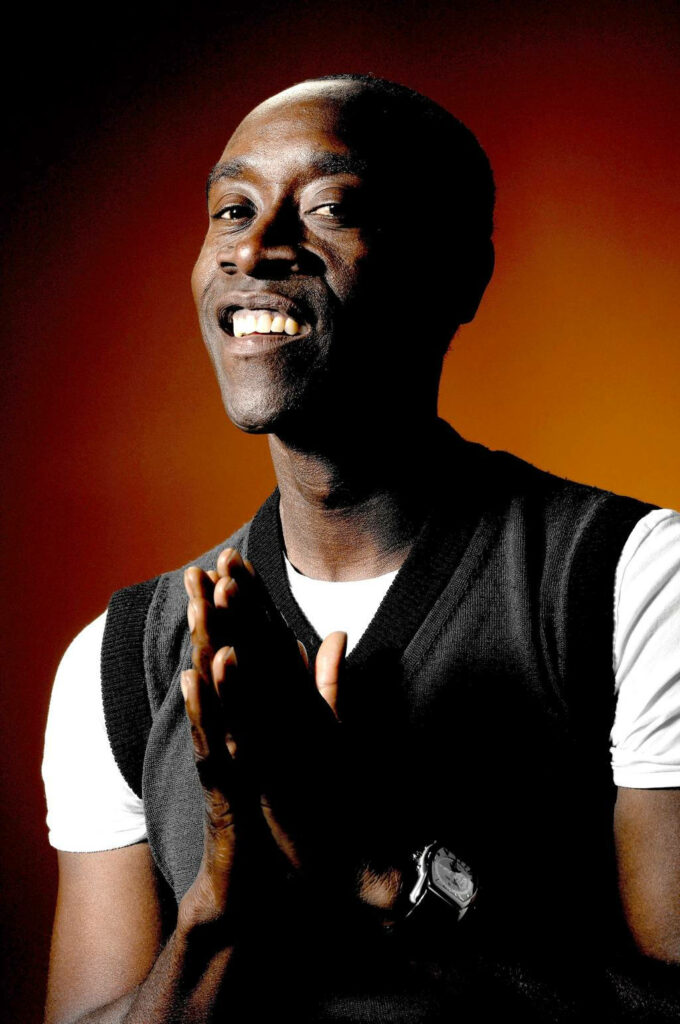 Portrait of Don Cheadle smiling in white t-shirt and black vest on warm orange gradient background Wallpaper