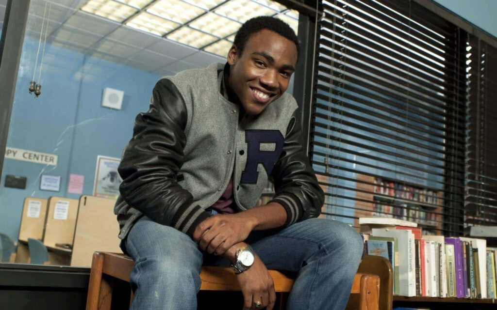 Donald Glover Smiling in Cozy Library with Stylish Varsity Jacket Wallpaper