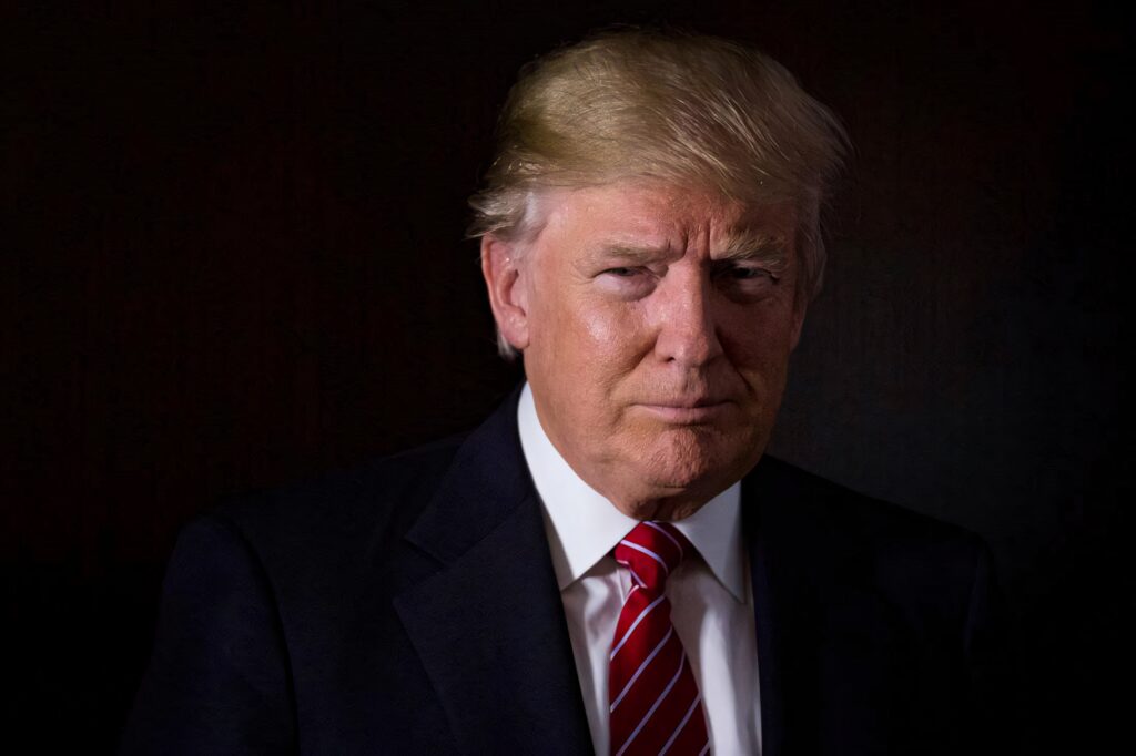 Donald Trump serious portrait in formal suit red striped tie dark shadowed background wallpaper