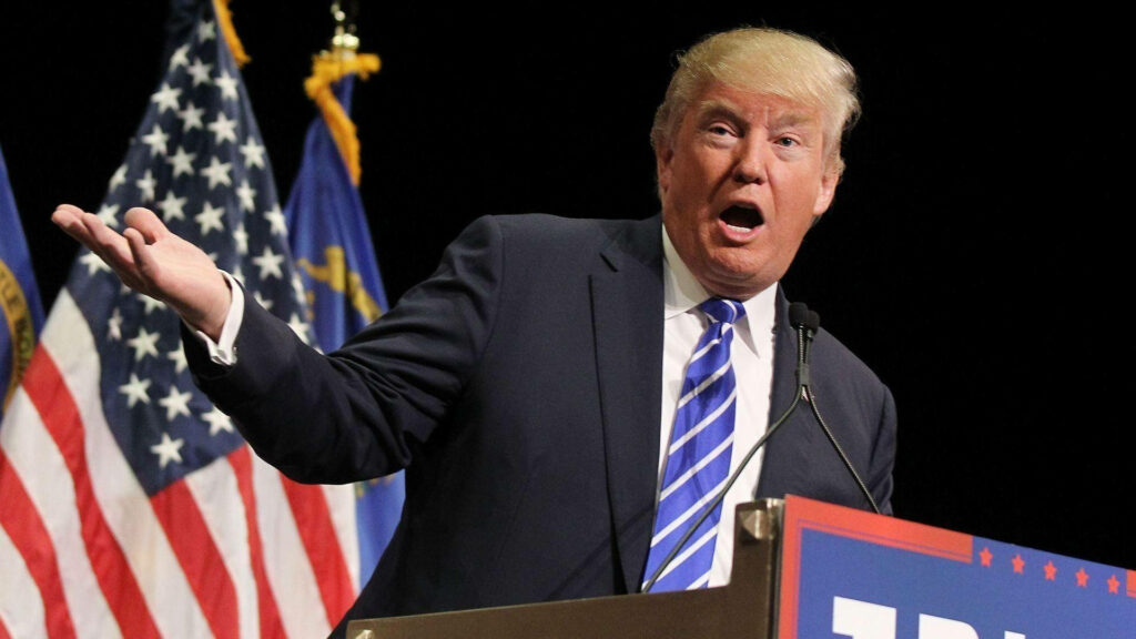 Donald Trump speaking mid-speech with expressive gestures American flags background wallpaper
