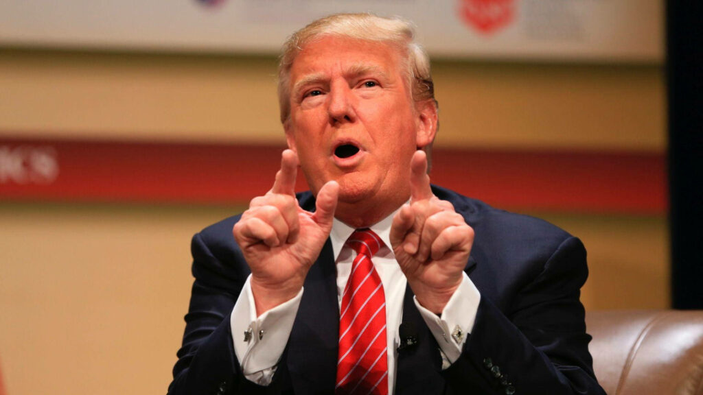 Donald Trump in navy suit red striped tie speaking with hand gestures in formal setting wallpaper background