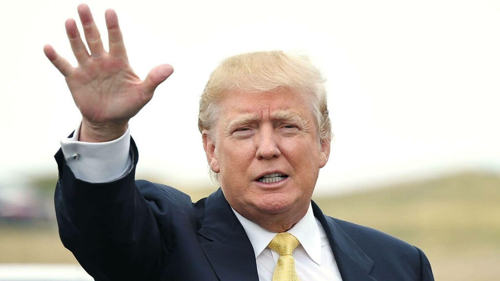 Donald Trump waving in an open field wearing dark suit white shirt yellow tie under bright sky Wallpaper