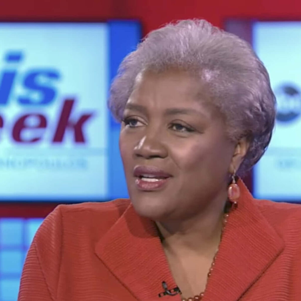 Donna Brazile speaking confidently in rust suit with red and blue TV studio background wallpaper