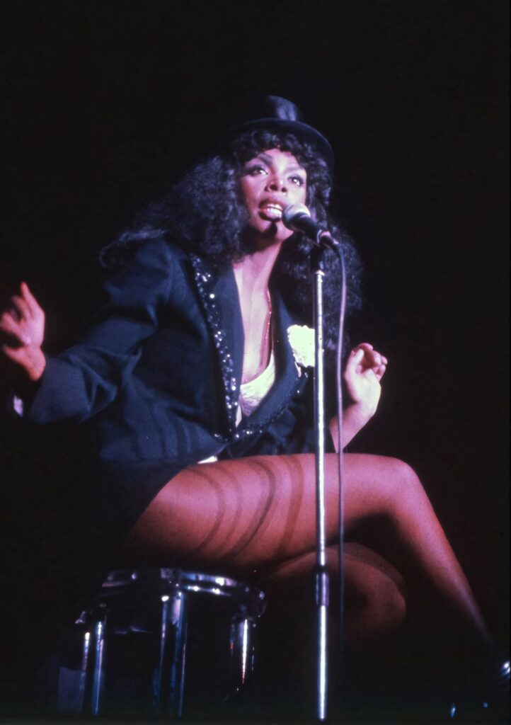 Donna Summer performing passionately in glamorous 1970s disco outfit with black jacket and top hat Wallpaper