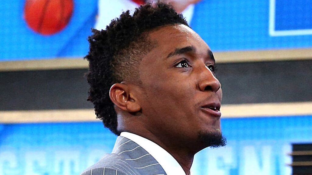 Donovan Mitchell in sharp pinstriped suit at formal sports event with blue dynamic background Wallpaper